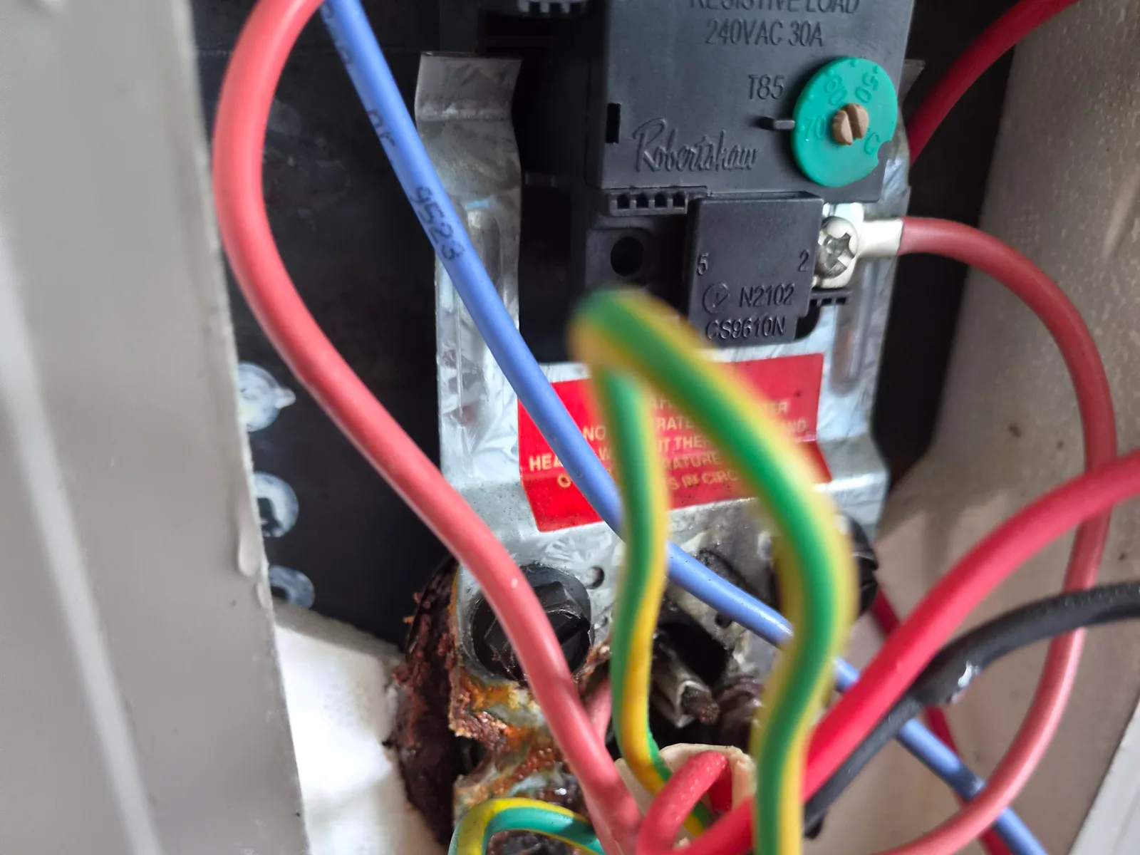 A corroded element terminal and thermostat wiring inside the access panel of an electric storage hot water tank, photographed by RCM