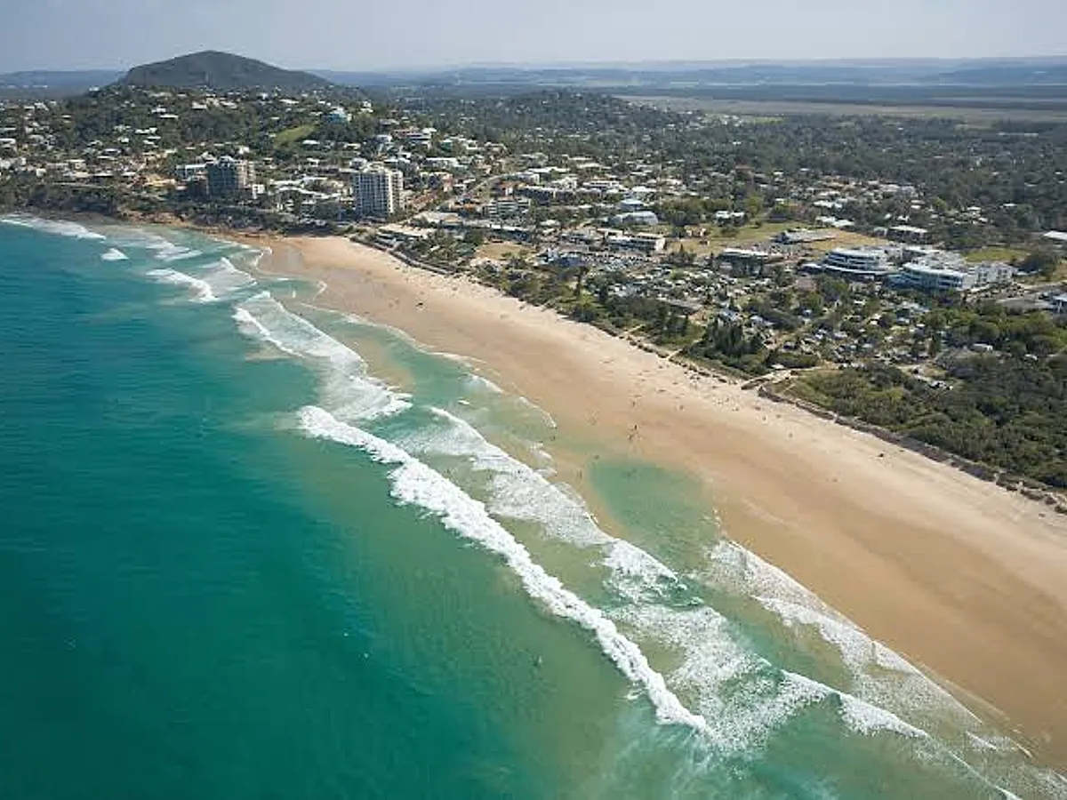 Aerial view of a Sunshine Coast beach town, with surf, sand and the suburb behind