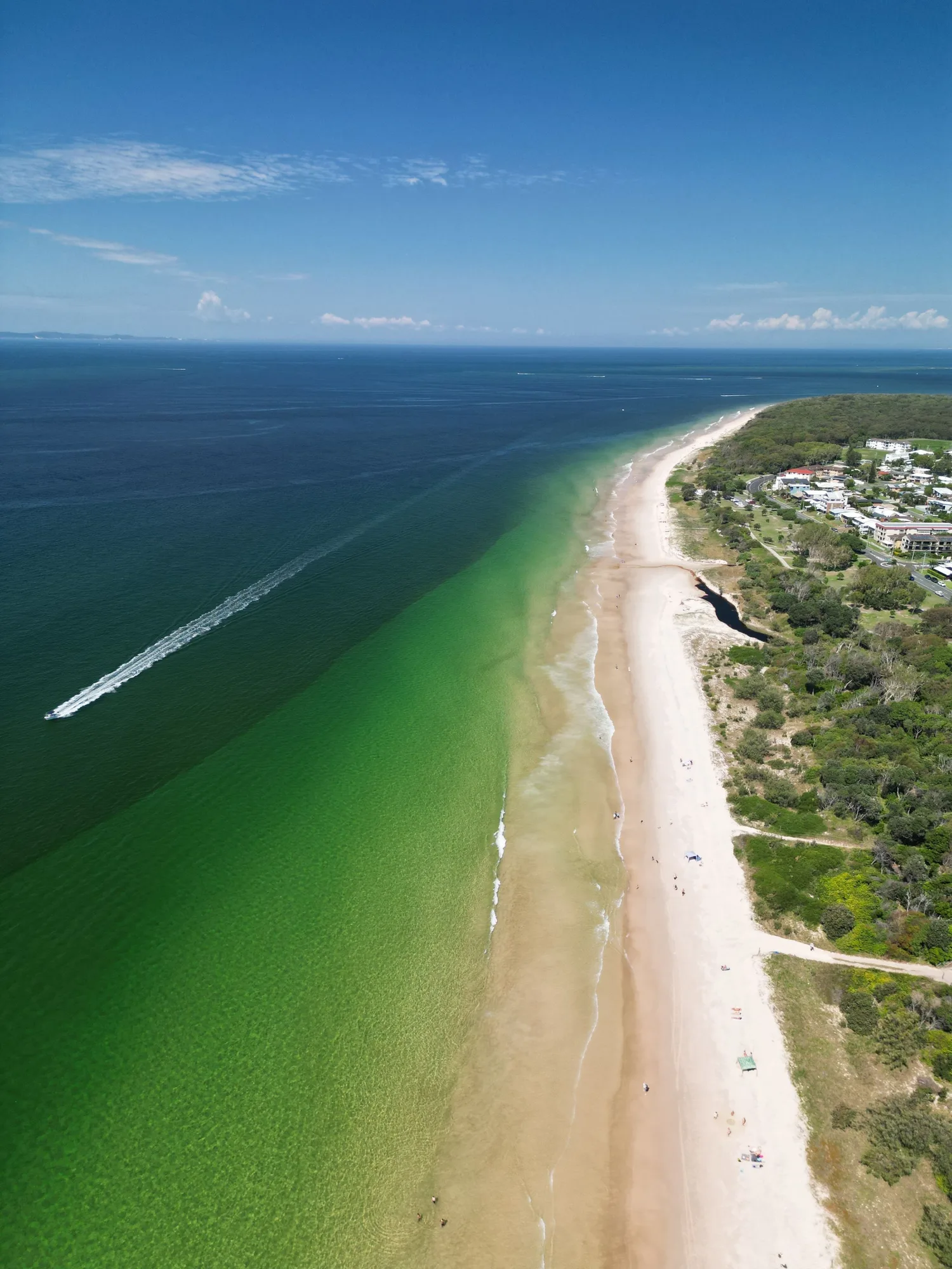 Aerial view of a long sandy beach, clear water and coastal bushland